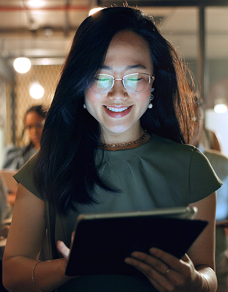 A young woman smiles as she works on a tablet.