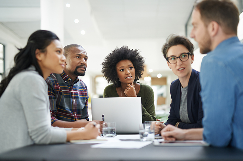 A group of young interns discusses a project around a table in an office.