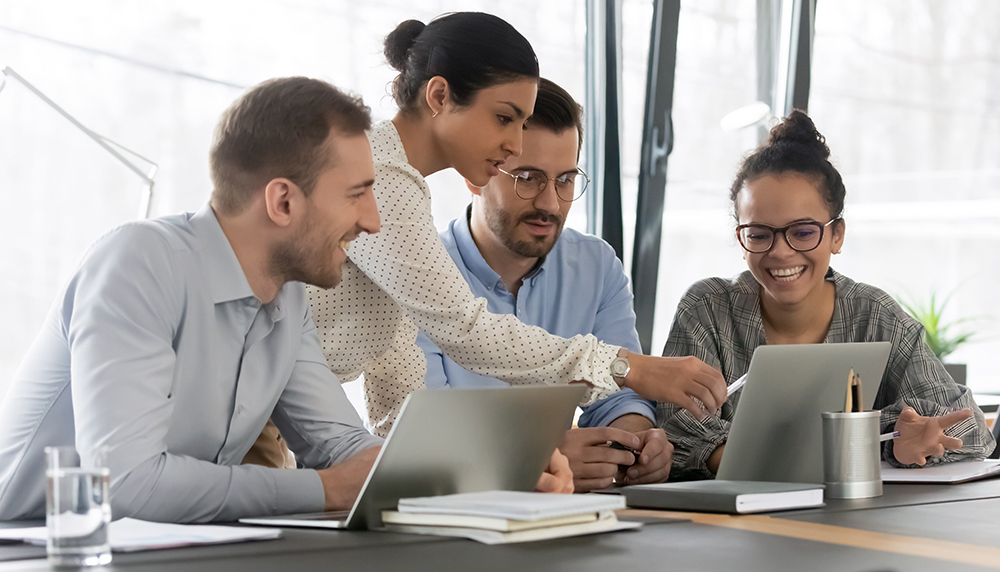 A young woman points at a computer in an office while three other interns look on.